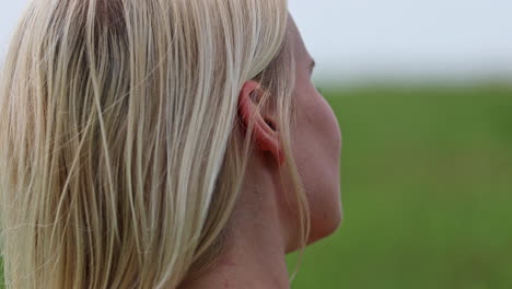 Rear-close-up-shot-of-blond-woman-standing-outside-on-green-meadow-during-daytime