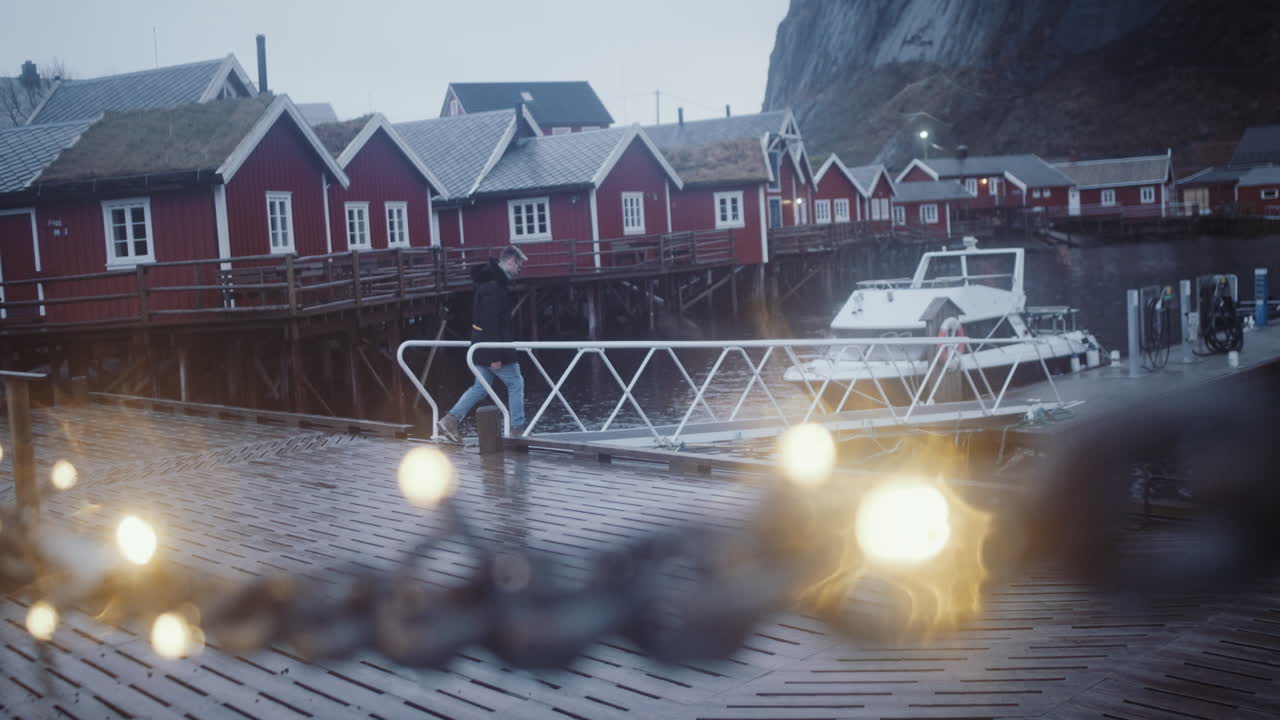 Young man walks on winter illuminated pier in Reine village, Lofoten, Norway