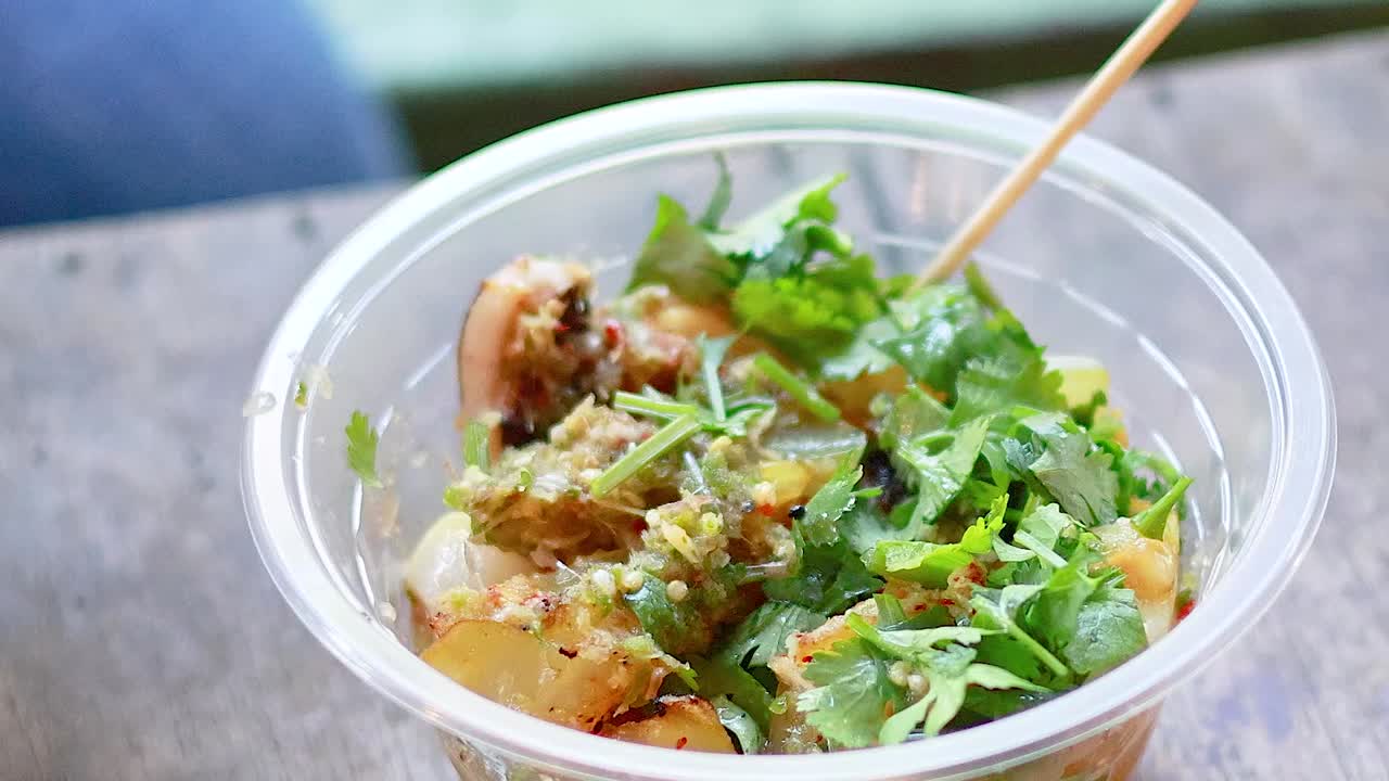 プラスチックのボウルから、木の串を使ってイカ焼きを拾い上げる人