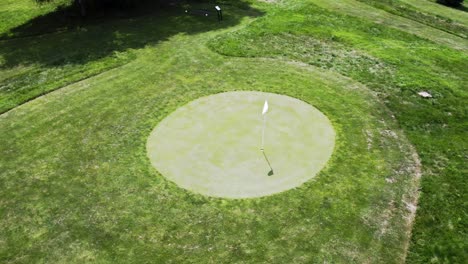 circular putting green and golf course hole with windblown flag, drone