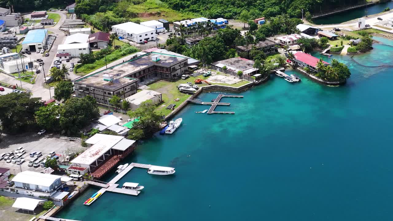 Inquadratura aerea con drone che spazia su un porto tropicale con acqua turchese ed edifici costieri
