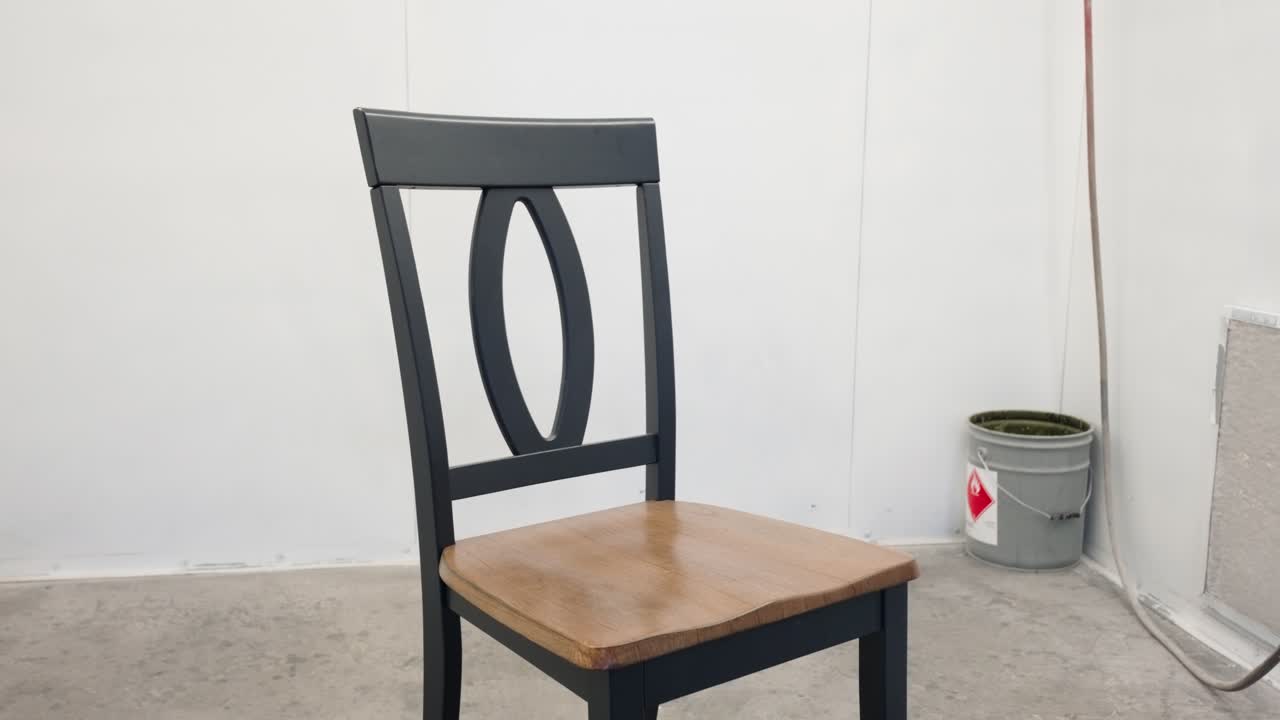 Upward pan reveals entire grey wooden chair inside professional paint booth
