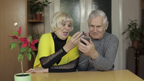 Pretty-mature-senior-couple-grandparents-enjoy-online-shopping-on-phone-at-home