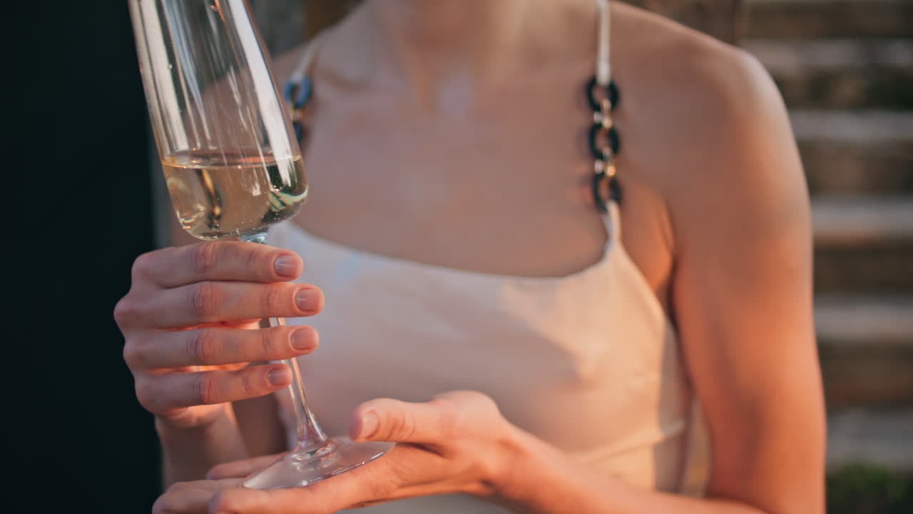 Primo piano di mani femminili che reggono un calice con una bevanda alcolica raffinata all'aperto.