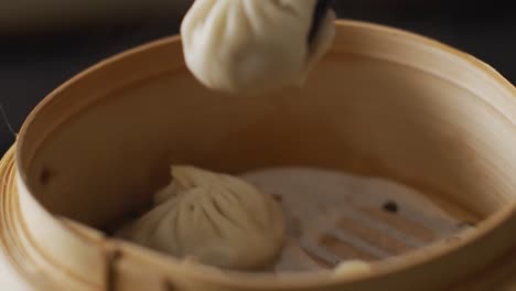 palillos con dumplings de dim sum en un vapor de bambú sobre un fondo negro