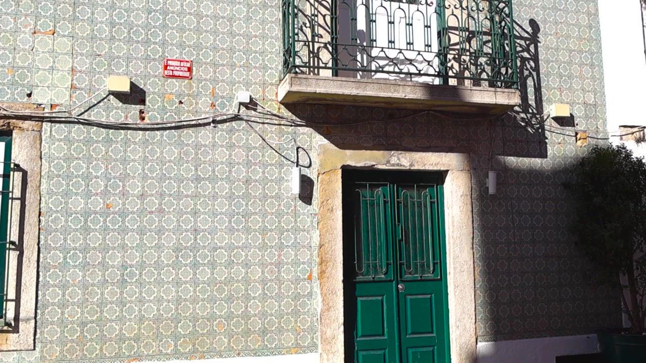 Lizbon'da, karmaşık Azulejo seramik fayanslara, klasik yeşil ahşap bir kapıya ve hareketli güneş ışığı ile gölgelerin düştüğü süslü bir balkona sahip geleneksel bir Portekiz binasının otantik cephesi.