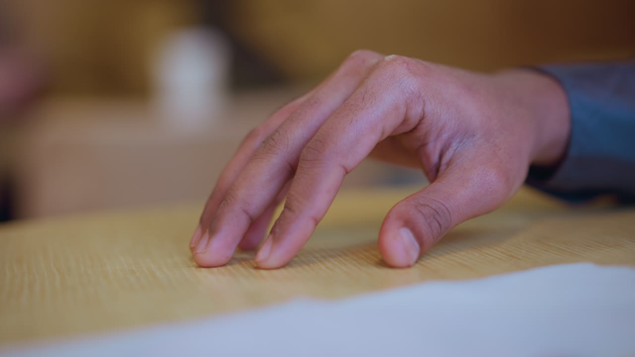 Close-up of young man's hand resting gently on wooden table near white napkin environment
