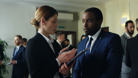 Caucasian-businesswoman-holding-documents-and-talking-with-an-African-American-colleague-discussing-something-in-the-hall-at-the-meeting