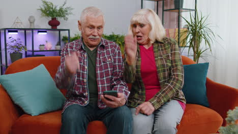 Overjoyed-grandmother-grandfather-hold-smartphone-excited-about-mobile-app-sport-bet-bid-win-at-home