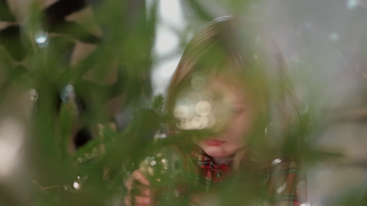 близкий мечтательный кадр маленькой девочки, украшающей рождественскую елку с семьей