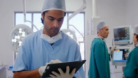 Chirurg-Nutzt-Digitales-Tablet,-Während-Kollegen-Im-Hintergrund-Interagieren