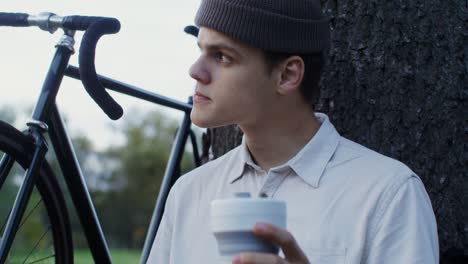 young man relaxing in a park with a coffee and bike