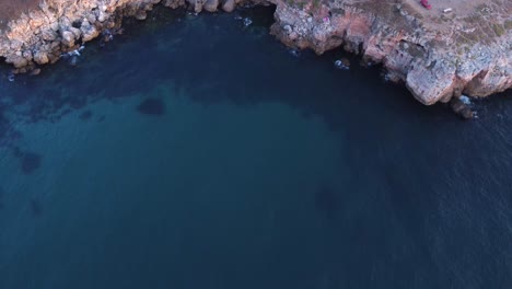 Top-down-aerial-view-of-waves-splash-against-rocky-seashore,-background