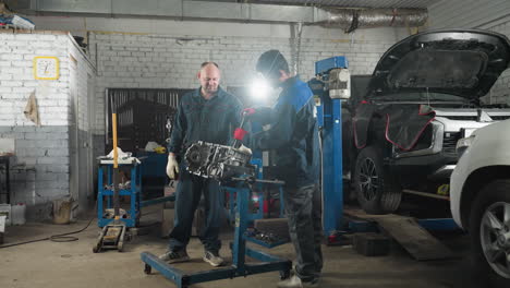 two mechanical engineers in an automotive workshop, one working on a car engine while the colleague observes, background features parked cars, mechanical tools, and workshop equipment