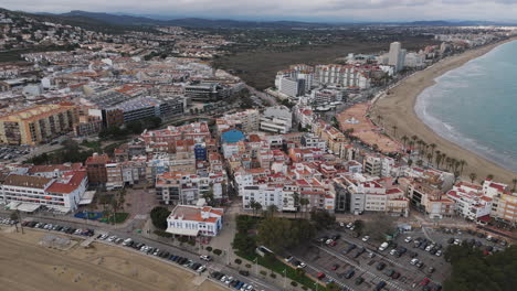 drone flies over town rooftops and coastline of peniscola with beach stretching below