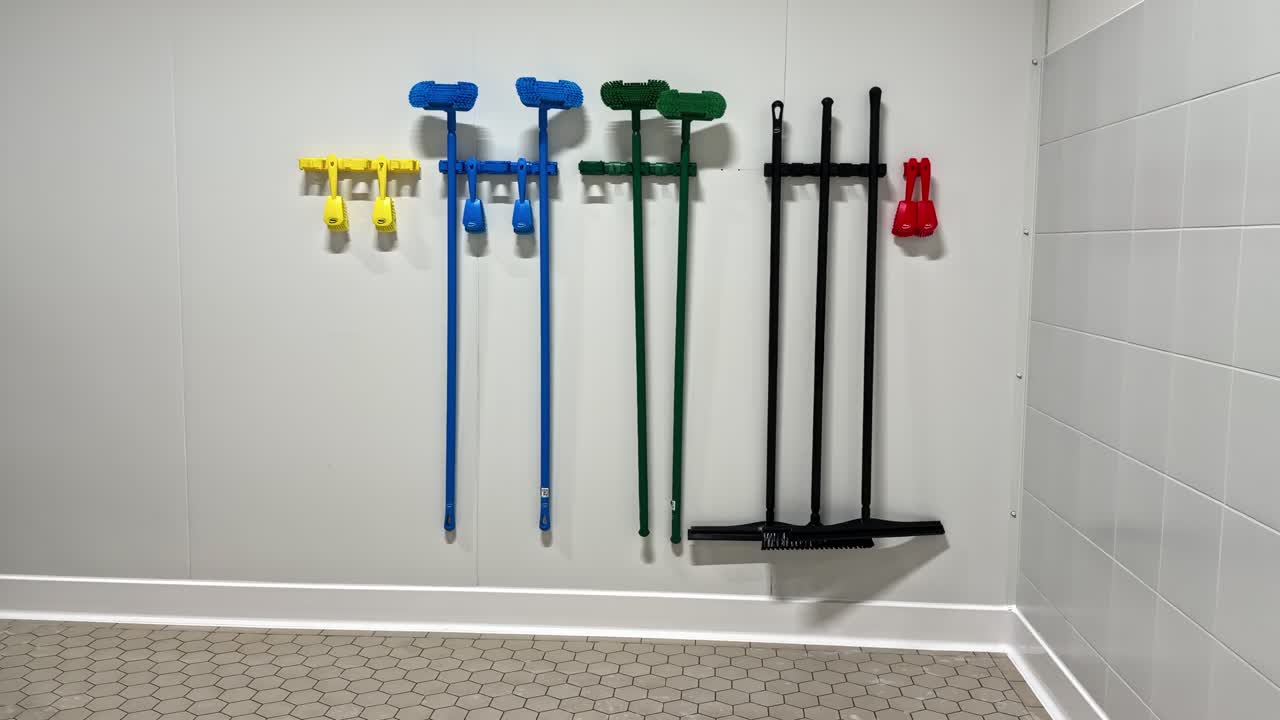 Color-coded cleaning tools organized on wall hooks in sanitized food processing environment
