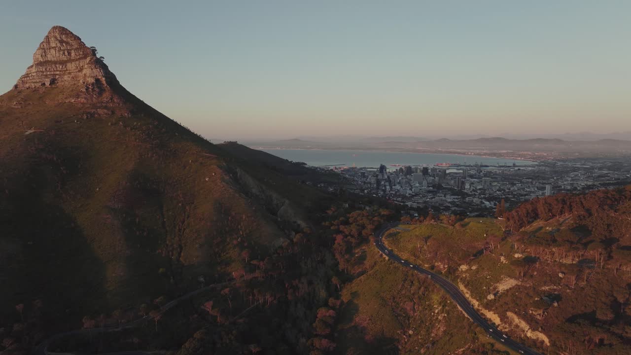 el dron vuela lentamente hacia el pico de la montaña de la cabeza del león - están iluminados por la luz del atardecer - en el valle se puede ver ciudad del cabo, sudáfrica - vista panorámica del mar abierto