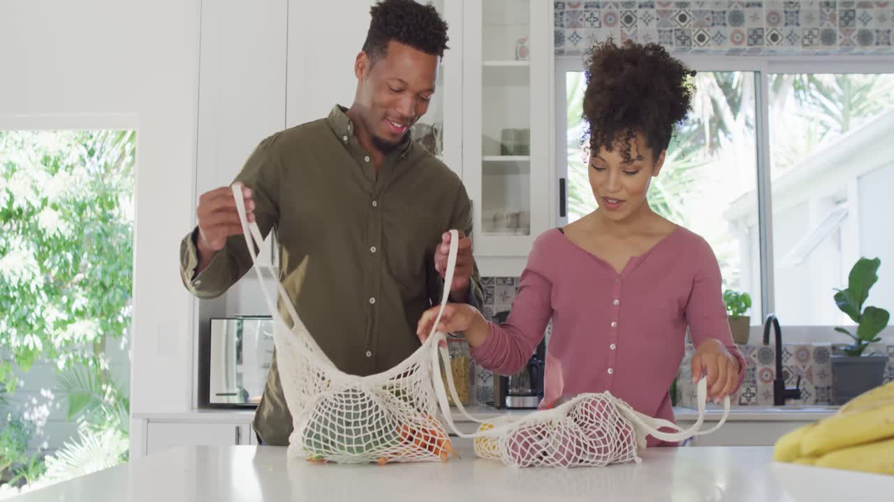 casal feliz afro-americano com sacos de vegetais na cozinha