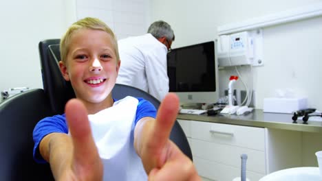 smiling young patient sitting on dentists chair showing thumbs up