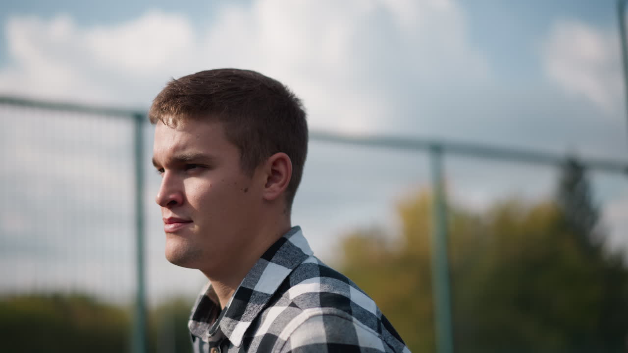 배경에 흐릿한 배구망과 울창한 초록색이 있는 야외 코트에서 칠색 셔츠를 입고 조하는 남자의 클로즈업, 신선한 공중에서 신체 활동 중에 움직임과 에너지를 포착합니다.