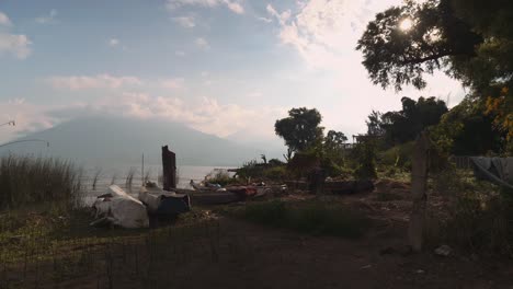 Kleine-Boote-Am-Ufer-Des-Atitlan-Sees-Bei-Sonnenaufgang-Mit-Wolkenbedecktem-Vulkan-Im-Hintergrund