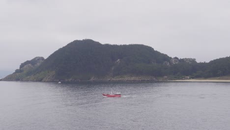 un barco rojo que pasa por una malhumorada y misteriosa isla deshabitada en la cadena de islas cies, españa