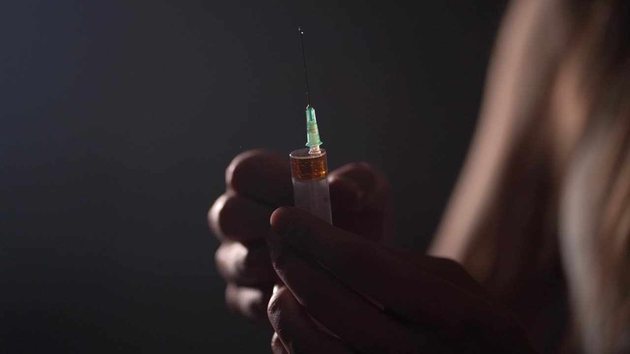 primer plano de una persona que prepara una jeringa desechable moviéndola con los dedos en cámara lenta y el líquido salpicando