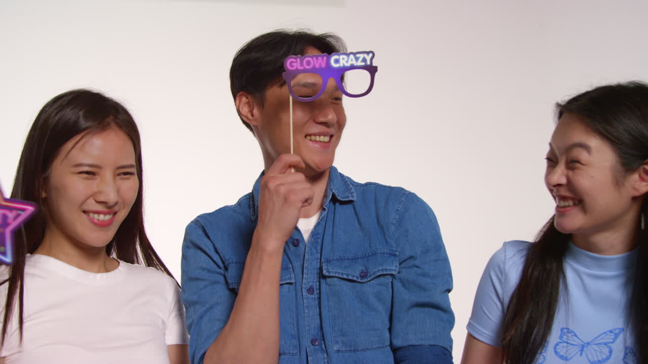 grupo de amigos jóvenes frente al fondo blanco del estudio divirtiéndose posando para retratos de estilo de cabina de fotos con accesorios 1