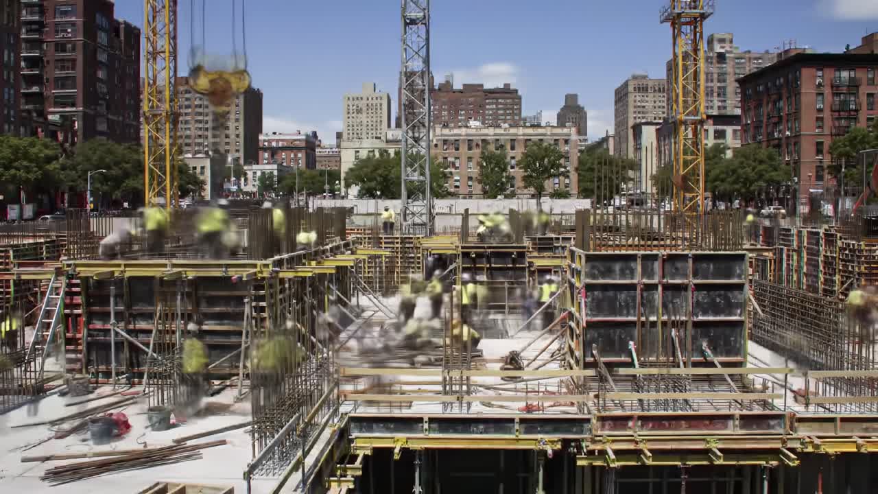 A busy construction site reveals workers collaborating to erect a large commercial building in a vibrant city. Skylines loom, and the project progresses under clear skies.