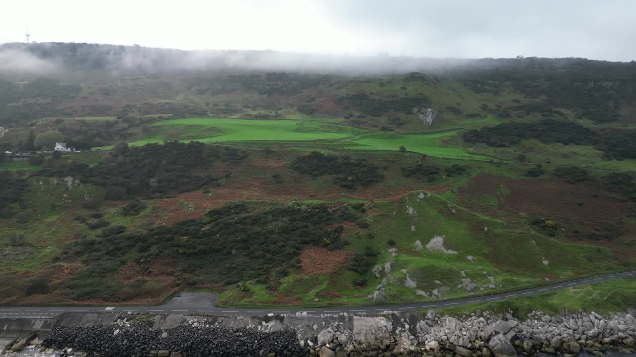 fotografía aérea al revés que revela el paisaje prístino de irlanda del norte con vistas a la carretera costera cerca de la ciudad de glenarm, mar tranquilo con aguas reflectantes y rocas en el agua en una mañana de otoño