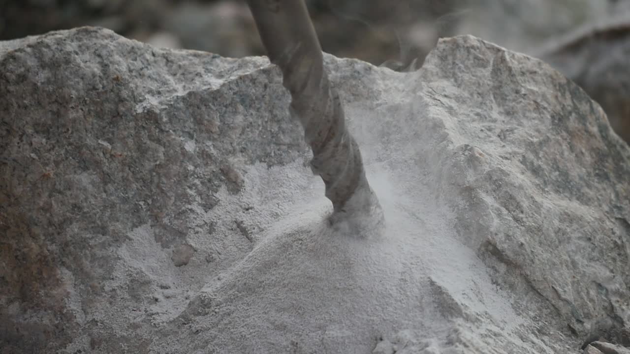 Close up of a driller digging a hole into a rock in slow motion producing smoke and sand