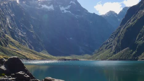 wide shot of idyllic lake marian with sun reflection of water surface surrounded by massive mountains in fiordland national park during summer