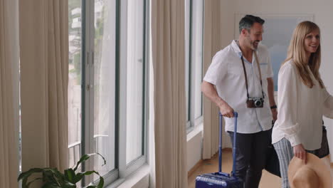 happy-travel-couple-arriving-in-hotel-room-on-honeymoon-vacation-looking-out-window-enjoying-beautiful-view-of-ocean-at-sunset-embracing-sharing-romantic-holiday