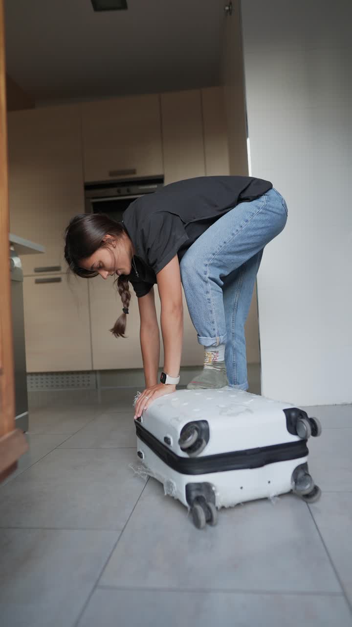 mujer luchando para levantar una maleta en una cocina