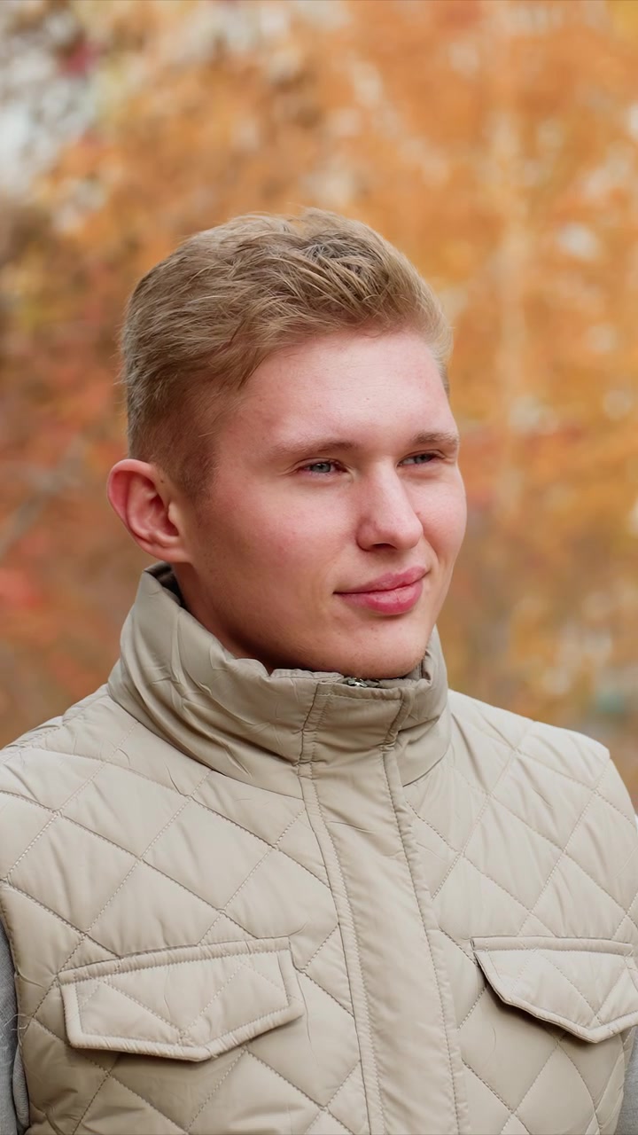 Kaukasialainen mies, jolla on lyhyet tummanvaaleat hiukset, ulkoiluvaatteissa. Vaatetukseen kuuluu harmaa aluspaita beigenvärisen takin alla. Valaistus viittaa myöhäiseen iltapäivään tai varhaiseen iltaan.