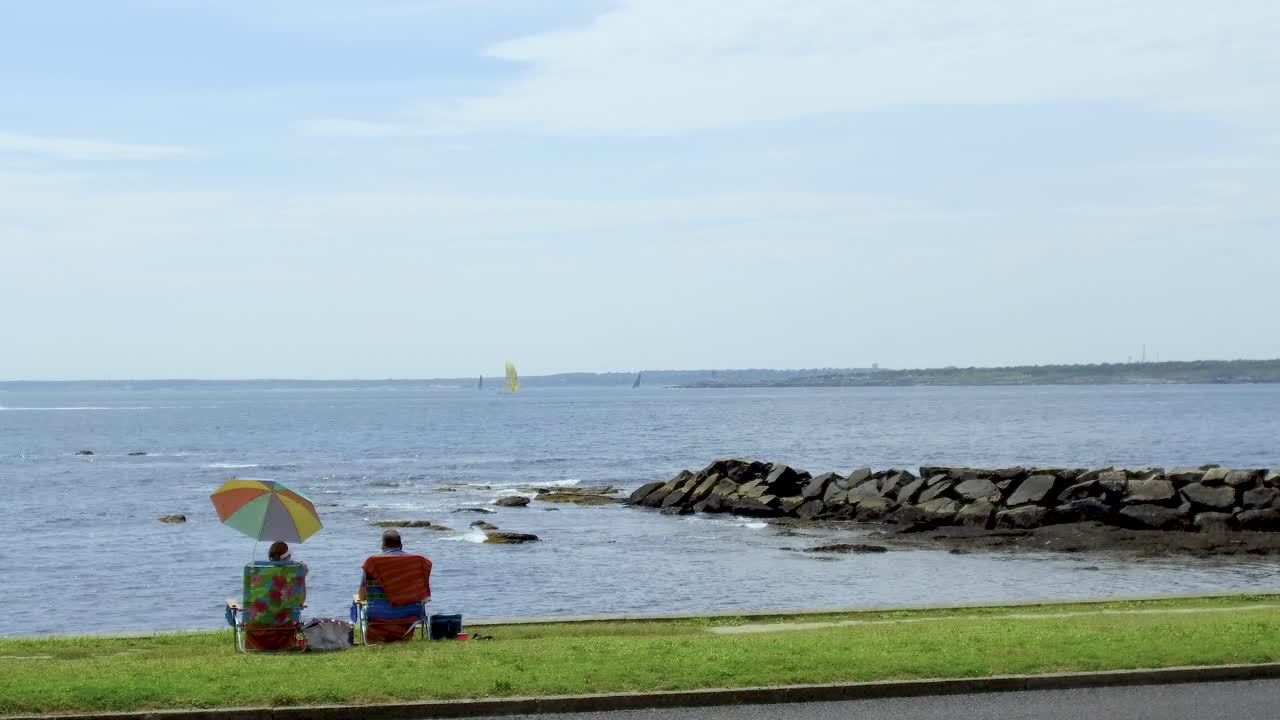 다채로운 우산 아래에서 전망을 즐기는 바다 앞 의자에 앉아 있는 커플