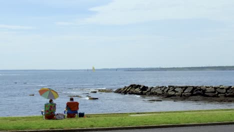 a couple sitting in chairs by the ocean front enjoying the view under a colorful umbrella