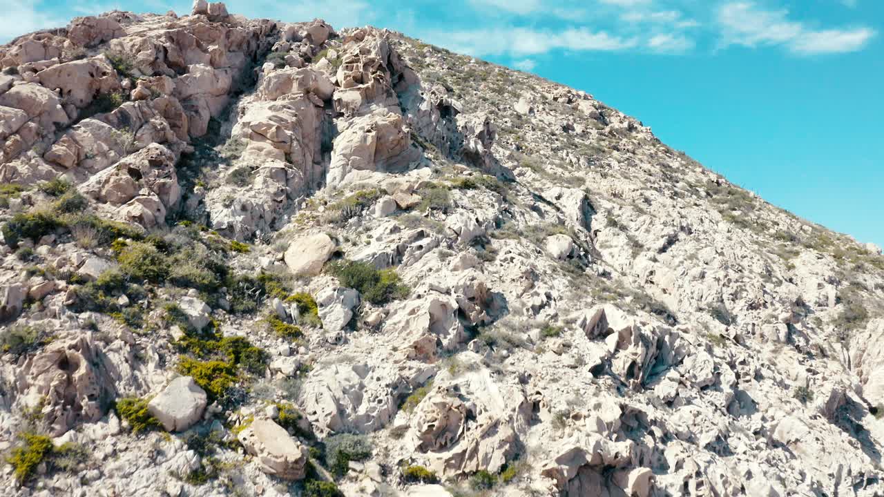 una impresionante toma aérea de un dron que sube a la cara de una gran montaña rocosa del desierto mientras las águilas vuelan por encima