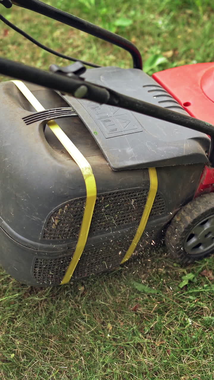 Boy working in the yard with lawn mower. Electric machine is cutting grass in the garden. Gardening works outdoors. Vertical video