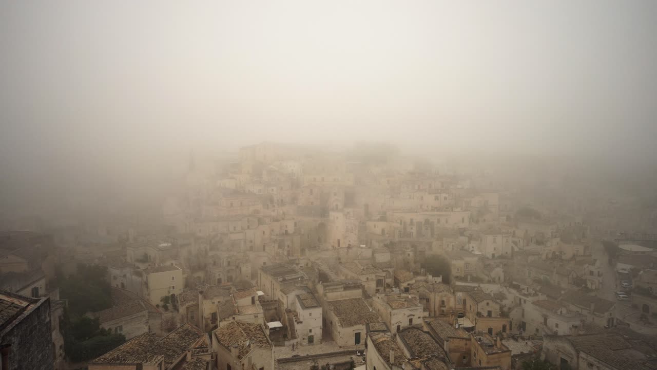 Lenta panoramica a sinistra che riprende la città vecchia di Matera avvolta nella nebbia, in 4k