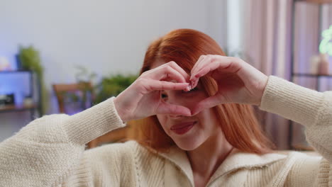 young woman making a heart shape with her hands, smiling and looking at the camera