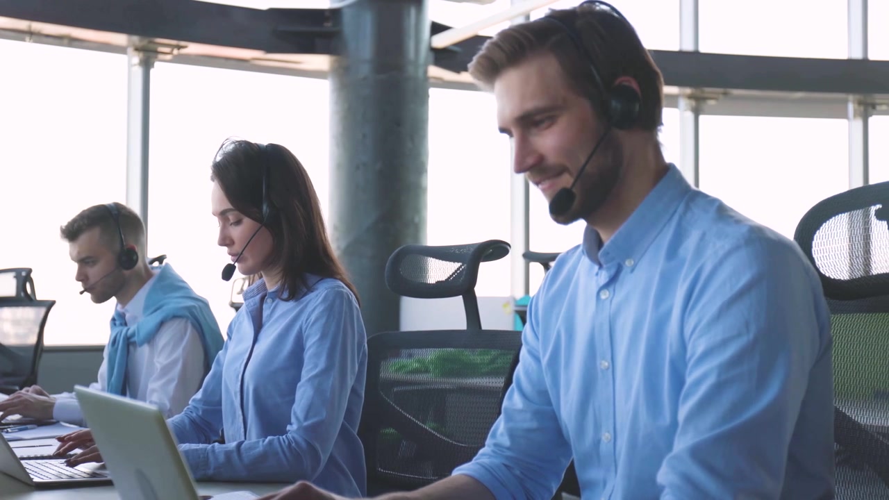 Smiling Call Center Agent Working on Laptop with Headset in Office