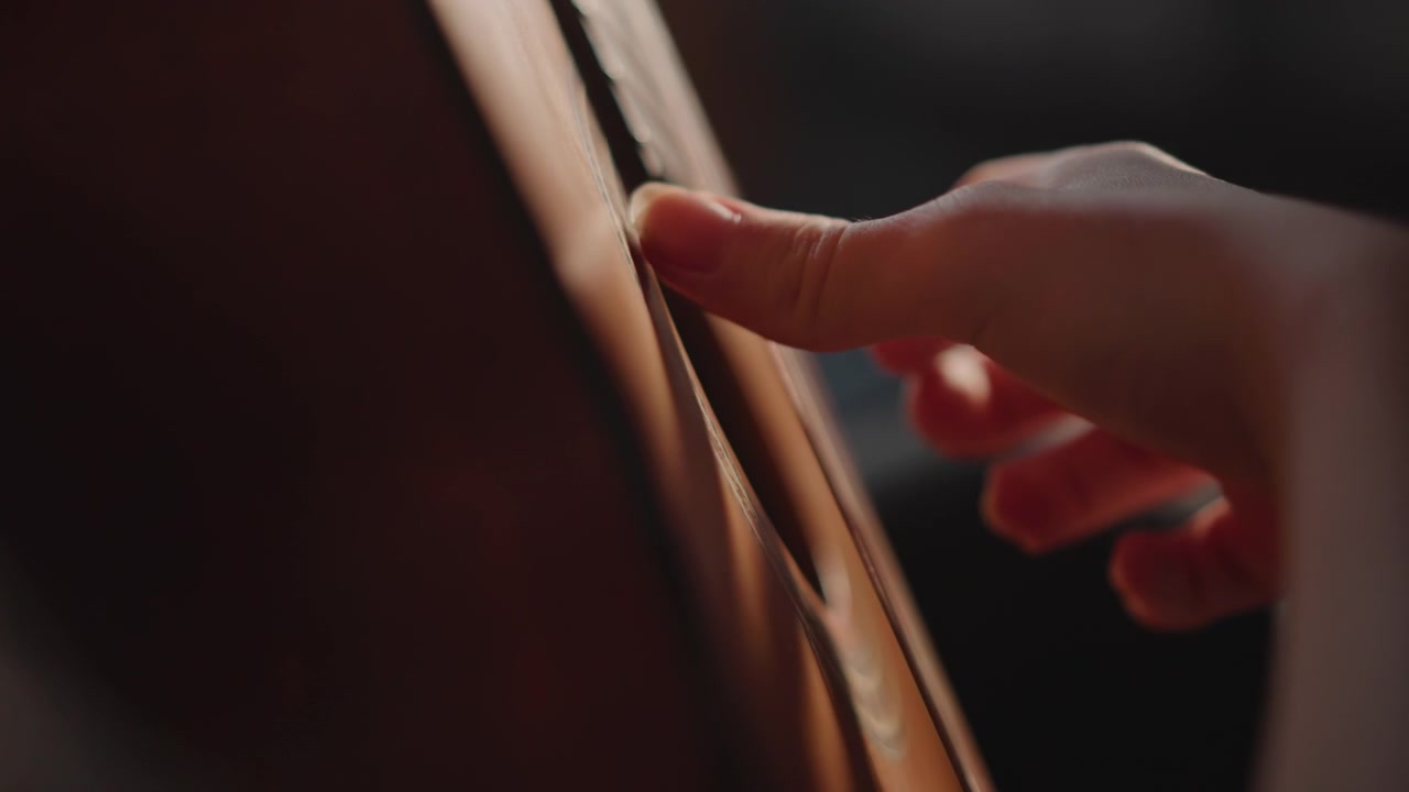 Jeu aux doigts en gros plan sur les cordes, coups d'ongles délicats créant des lignes mélodiques, vue détaillée du manche et du mouvement de la main, séance de pratique intime avec lumière chaude et flou artistique