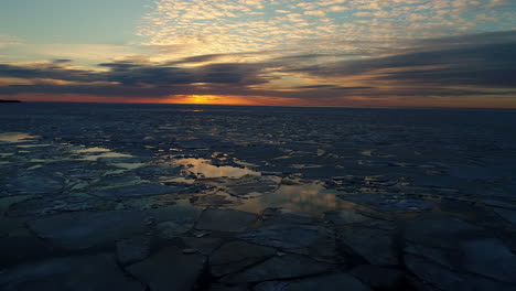 aerial flyover baltic sea with swimming ice floes on water surface during sunset at horizon