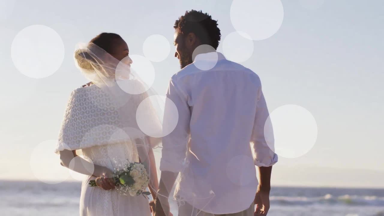 Animation of light spots over african american couple getting married on beach