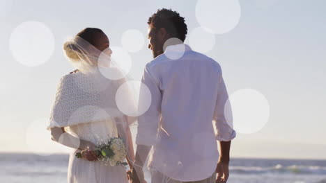 Animation-of-light-spots-over-african-american-couple-getting-married-on-beach