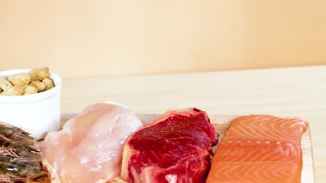 a variety of protein-rich foods including meats, fish, and nuts are neatly arranged on a wooden surface under bright lighting