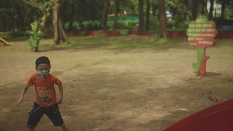 a 7-second clip a young boy wearing an orange shirt and black shorts, sliding down a red slippery slide he jumps up, pulls up his pants, and runs back to slide again