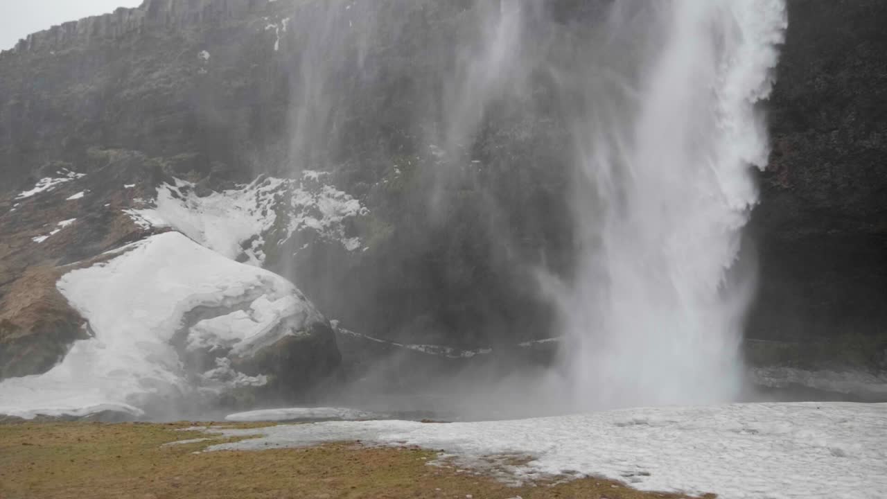 toma estática y lenta de agua golpeando el suelo nevado, en la cascada de skogafoss, en un día nublado de otoño, en islandia