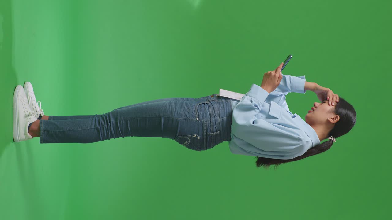 전체 몸의 측면 뷰 아시아 사업가 여성은 만족하지 않고 녹색 화면 스튜디오에서 휴대 전화를 사용하는 동안 머리를 흔들고 있습니다.